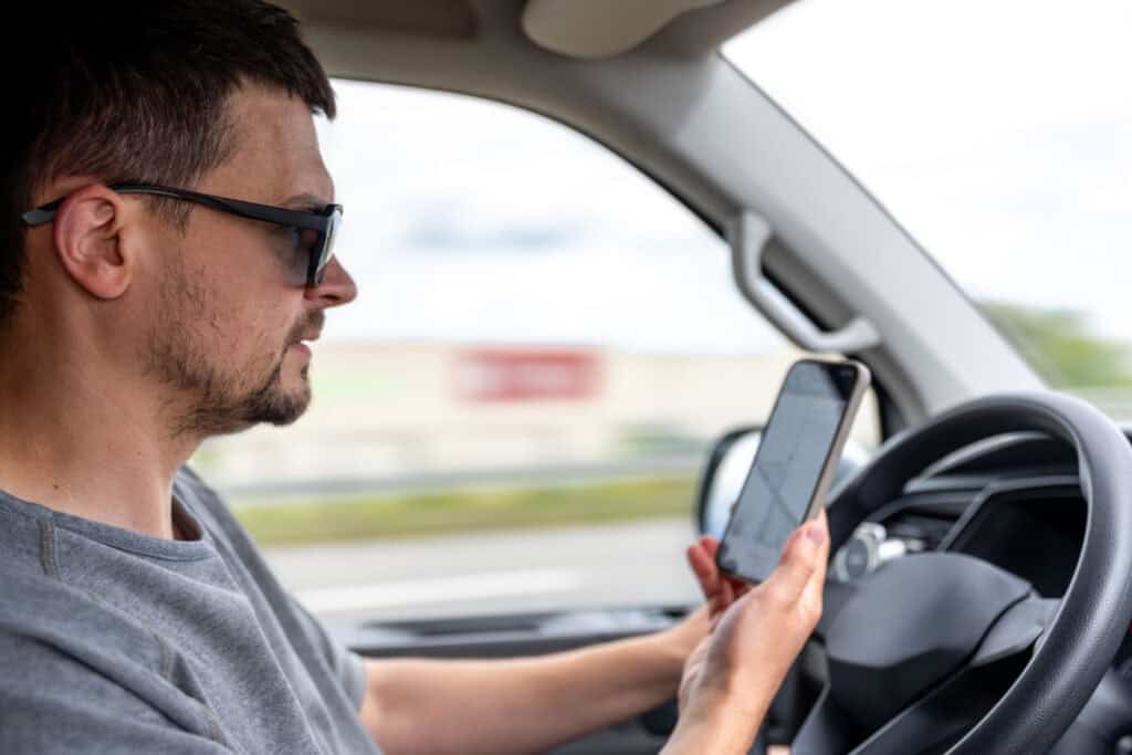 A photo of a man driving a car while distracted by his phone, highlighting Oklahoma’s new distracted driving law.