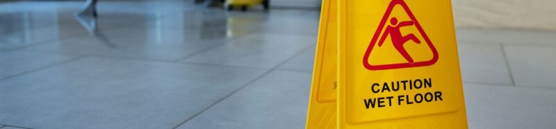 Fotografía de un suelo mojado y un cartel de advertencia que indica el riesgo de resbalones y caídas.