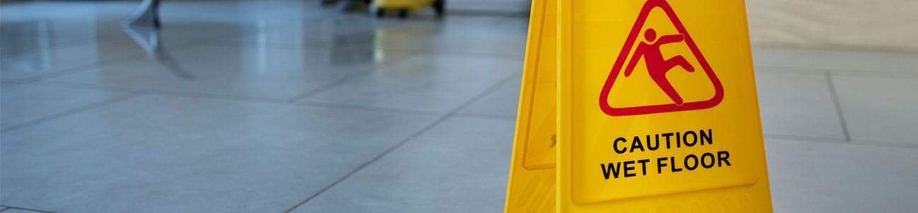 Fotografía de un suelo mojado y un cartel de advertencia que indica el riesgo de resbalones y caídas.